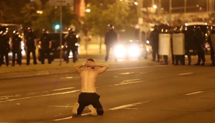 <p>Białoruś. Mężczyzna klęczący przed kordonem policjant&oacute;w</p>