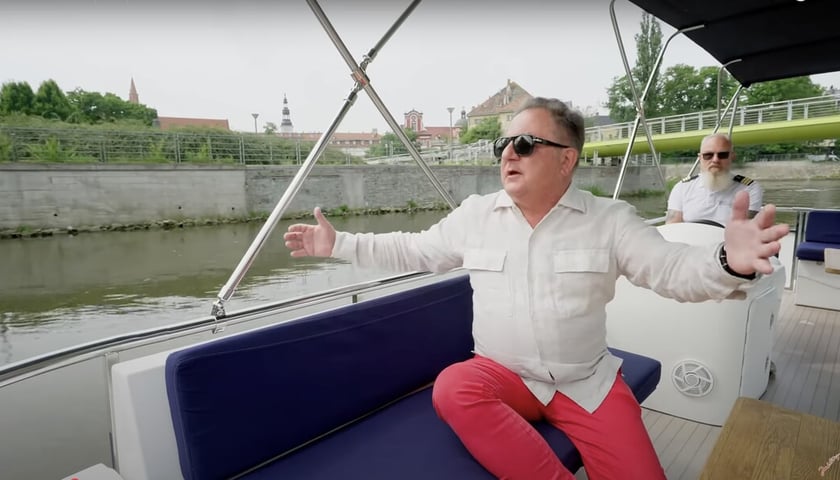 Robert Makłowicz w białej koszuli i okularach słonecznych na łodzi płynącej Odrą