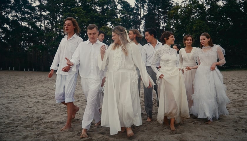 Bohaterowie "Trzech sióstr", spektaklu w szkole teatralnej we Wrocławiu. Na zdjęciu grupa młodych ludzi w jasnych kostiumach. 