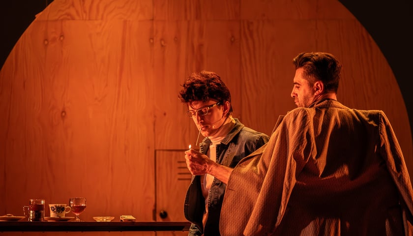 Lubiewo na scenie Wrocławskiego Teatru Współczesnego. Scena z próby spektaklu. Na zdjęciu dwóch mężczyzn, jeden przypala drugiemu papierosa