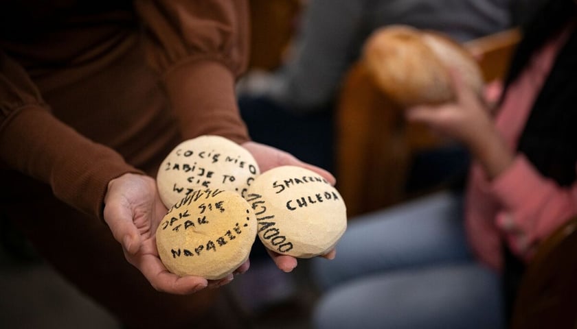 <p>ręce kobiety, trzymającej trzy kamienne bułki z podpisami</p>