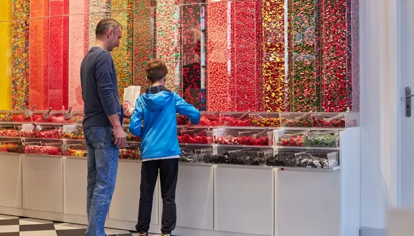 Na zdjęciu:  mężczyzna i chłopiec przed ścianą z cukierkami w nowym sklepie Sweet Factory Store we Wrocławiu