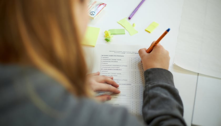 na zdjęciu ilustracyjnym kobieta siedząca tyłem, przed nią na stole leża zapisane kartki 