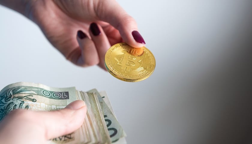 Na zdjęciu widać dłonie trzymające banknoty i bitcoin
