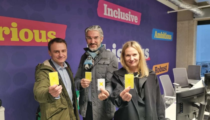 Na zdjęciu dwóch mężczyzn i kobieta, trzymają w dłoniach plakietki identyfikacyjne