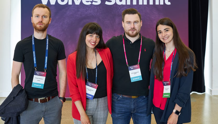 Czwórka uczestników Wolves Summit 2023 (dwie kobiety i dwóch mężczyzn). W tle nazwa festiwalu - biały napis na fioletowym tle