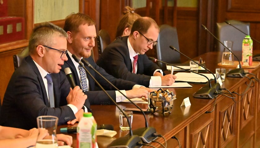 Trzech mężczyzn w garniturach siedzi przy podłużnym stole, przed nimi stoją mikrofony, leżą notatniki. Delegacja Saksonii w Ratuszu 