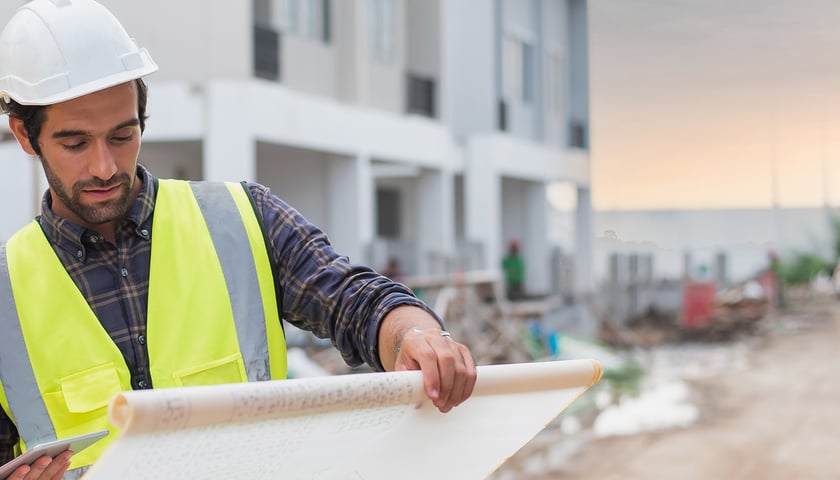 Mężczyzna w kasku z planami w rękach na budowie 