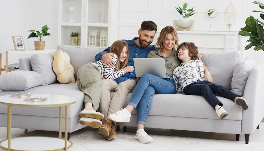 Kobieta, mężczyzna i dzieci w mieszkaniu, siedzą na sofie i patrzą na ekran komputera, zdjęcie ilustracyjne 