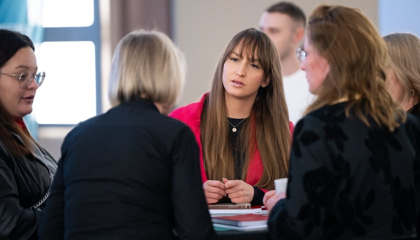 Pięć kobiet stoi wokół stołu (trzy ustawione są plecami). Przodem jest kobieta z długimi włosami i w czerwonym swetrze. Spotkanie „Bez Mikro Nie Ma Makro” w Żmigrodzie (11.01.2024)