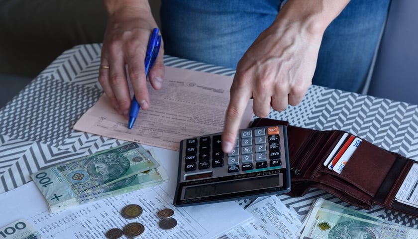 Na stole leżą pieniądze (banknoty 100-złotowe i monety), kalkulator, portfel i kartka papieru z decyzją o wysokości podatku od nieruchomości o charakterystycznym łososiowym kolorze (zdjęcie ilustracyjne)  
