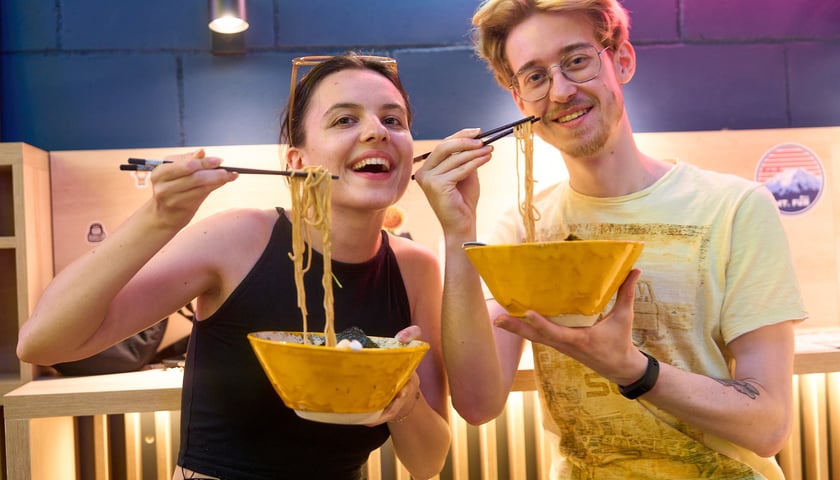 Goście Vegan AF Ramen w lokalu przy Oławskiej. Młoda, uśmiechnięta kobieta i mężczyzna z miskami ramenu.