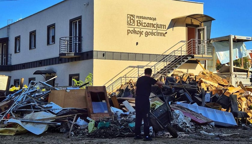 Mężczyzna z taczką, w tle zniszczone meble i budynek z napisem Restauracja Biznancjum. Pokoje gościnne, Zniszczenia po powodzi na Dolnym Śląsku, 23 września 2024 r. 