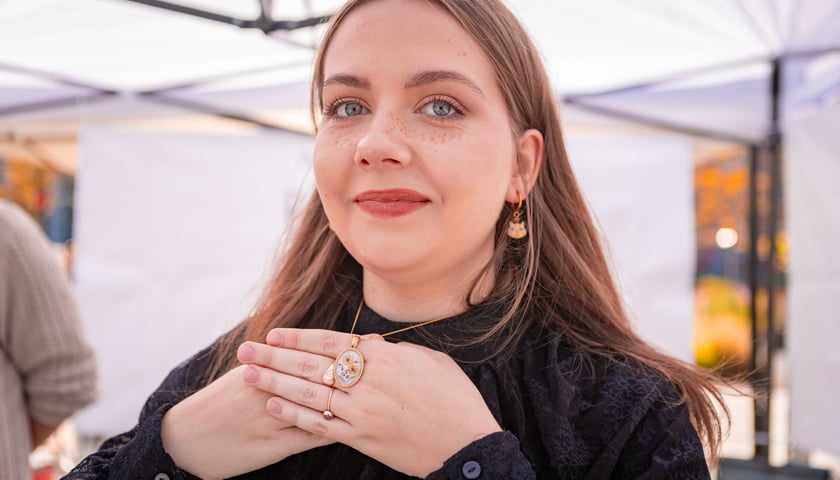 Uśmiechnięta dziewczyna w dłoniach ma zawieszką na łańcuszku, uczestniczka targów rzeczy niepospolitych Artishop na pl. Nowy Targ, 28.09.2025 r.