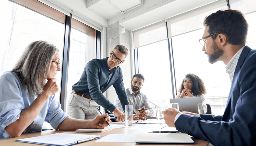 Dwie kobiety i trzech mężczyzn siedzą przy stole, na którym są dokumenty, zdjęcie ilustracyjne