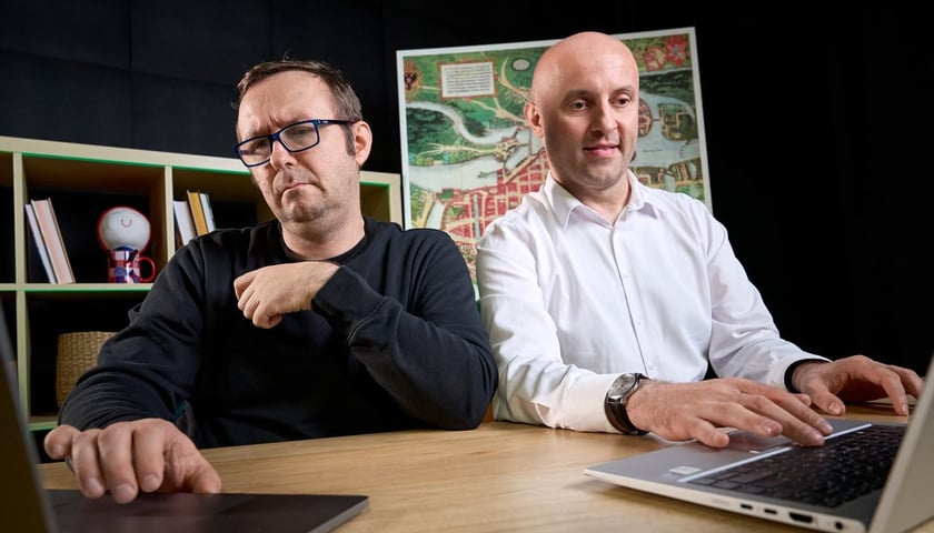 Dwóch mężczyzn siedzi przy stole, patrzą na ekrany laptopów. Od lewej strony siedzą: Bartłomiej Karaban i Łukasz Kmieć, liderzy WAIT – Wrocław AI Team. 