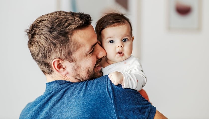 Młody mężczyzna trzyma dziecko na rękach, zdjęcie ilustracyjne. Pracujący rodzice dostaną z ZUS 1500 zł co miesiąc