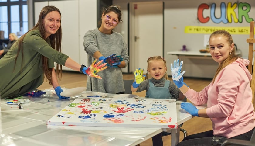Powiększ obraz: Warsztaty plastyczne w prowadzonym przez Fundację Ukraina Centrum Ukraińskiej Kultury i Rozwoju (CUKR). Na zdjęciu trzy kobiety i mała dziewczynka tworzące obraz przy pomocy zanurzanych w farbie dłoni.