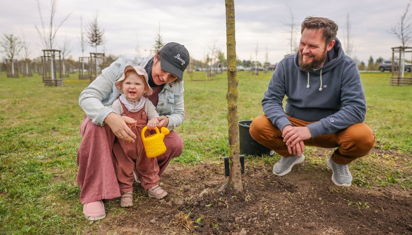 Piknik WROśnij we WROcław w powstającym parku przy ul. Rdestowej, uśmiechnięci rodzice z dzieckiem pozują przy swoim drzewku