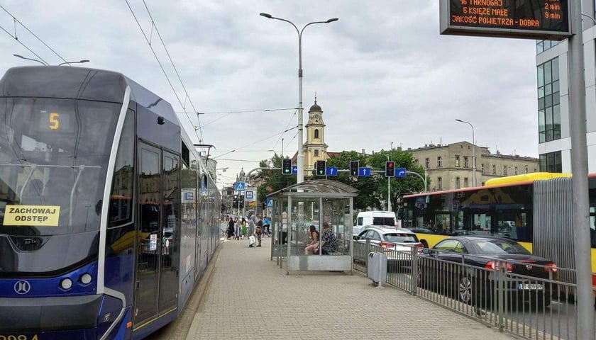 Przy przystanku Plac Wróblewskiego: tramwaj, pasażerowie, samochody, autobus, w tle wieża kościoła