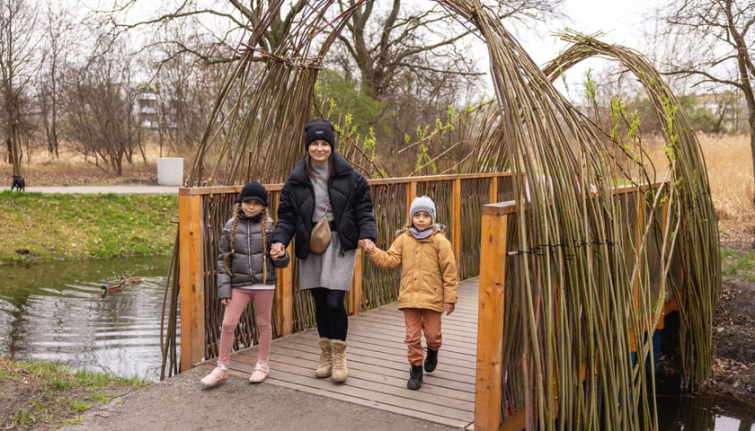 Kobieta z dwójką dzieci przechodzi przez mostek w parku Krzyckim