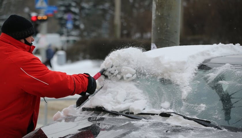 <p>Atak zimy we Wrocławiu. Mężczyzna w czerwonej kurtce odśnieżający samoch&oacute;d. Zdjęcie wykonane w lutym 2021.</p>