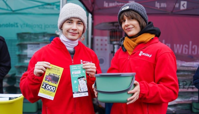 Mężczyzna i kobieta trzymający w rękach ulotki informacyjne i pudełko na bioodpady - akcja rozdawania pojemników przy ul. Zakładowej 20.12.2025