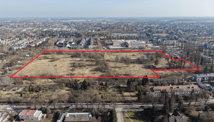 Widok z lotu ptaka na budynki, drzewa i tereny zielone - obszar między ulicami Ołtaszyńską i Zwycięską, który Wrocław ma otrzymać od AMW (oznaczony czerwona linią).