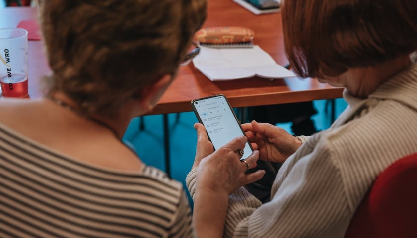Dwie kobiety siedzące tyłem do obiektywu patrzą na ekran telefonu komórkowego