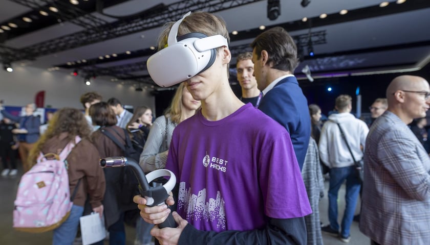 Młody mężczyzna w fioletowym podkoszulku ma założone gogle VR.