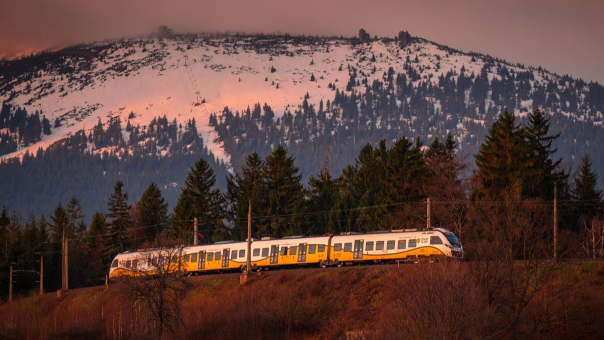 Pociąg Kolei Dolnośląskich na górskiej trasie. W tle ośnieżony stok.