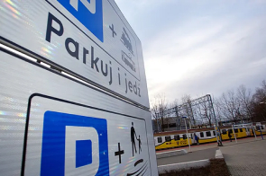 Na zdjęciu widnieje znak "Parkuj i jedź", a w oddali stacja kolejowa.